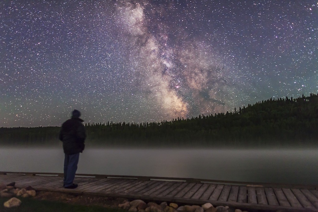 Me posing in the night at Reesor Lake, Cypress Hills Interprovincial Park, Alberta, with the Milky Way over the misty lake. A single 30-second untracked exposure (not a composite) with the 24mm lens at f/2 and Canon 5D MkII at ISO 3200.