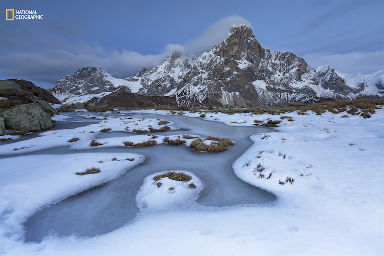 The first cold days of winter have frozen the surface of a pond. The first snowfall has revealed its delicate beauty. A long shutter speed enhances the movement of the clouds around Mt. Cimon de la Pala, Paneveggio-Pale San Martino Natural Park, Italy