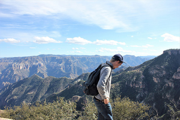 A young man stands in front of a sweeping mountain vista during a break from El Chepe train. 