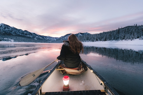 A woman paddling a canoe in the Canadian mountains, which is one of the best destinations to visit if you're going through a breakup.